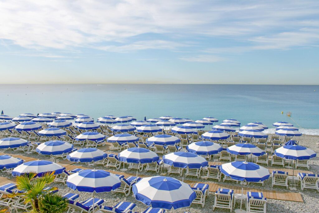blue and white stripped umbrellas on beach with sea on your one day in nice