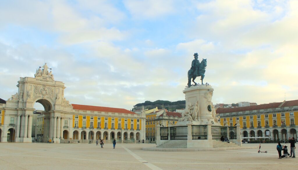 square with yellow arcade and large archway with statue of man on horse in lisbon
