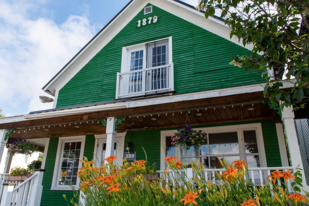 green wood house with white trim and orange flowers in Quebec village