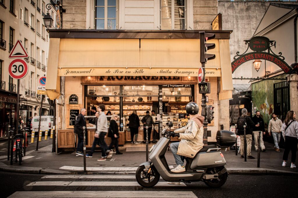 man on scooter in front of cheese shop on busy street in paris