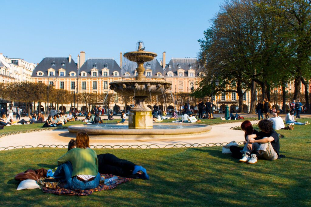 people on lawn with fountain and building in background a popular thing to do in Marais Paris