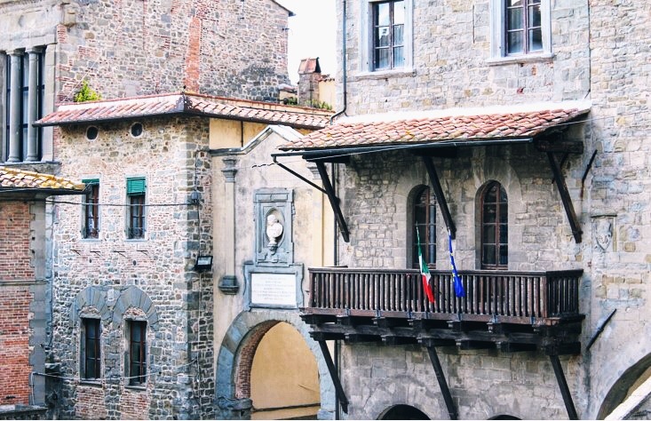 stone building with wooden balcony and flags in cortona
