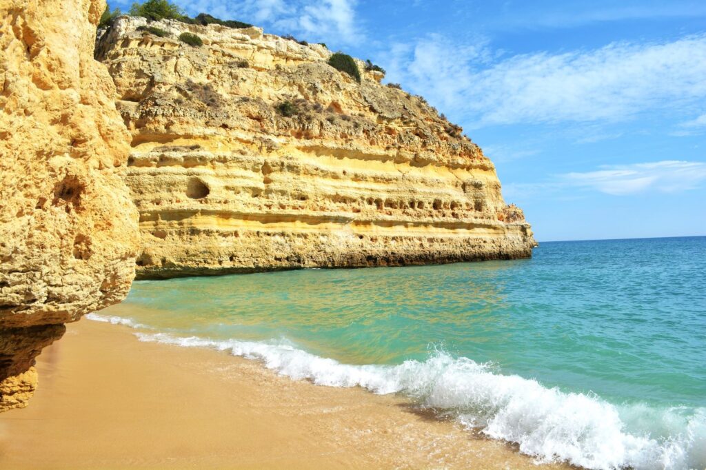 yellow rock formation with turquoise water on beach in algarve