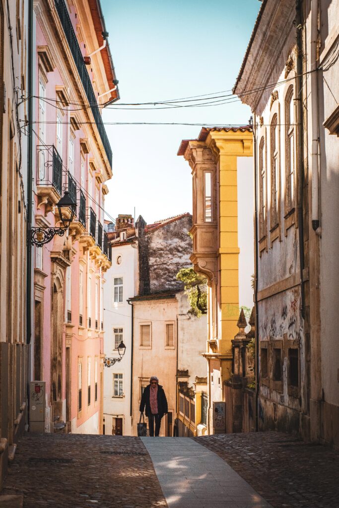 woman walking on cobblestone alleyway with tall buildings in the historic city of coimbra in portugal