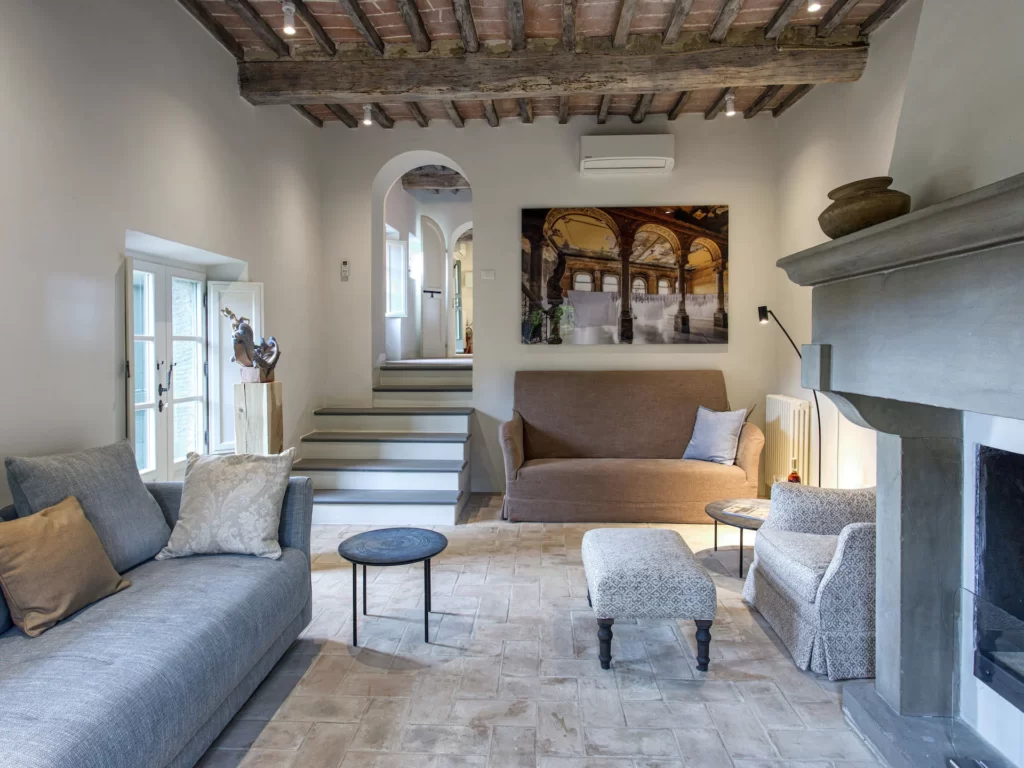gray sofa, stone fireplace with beamed ceiling and artwork in cortona villa 
