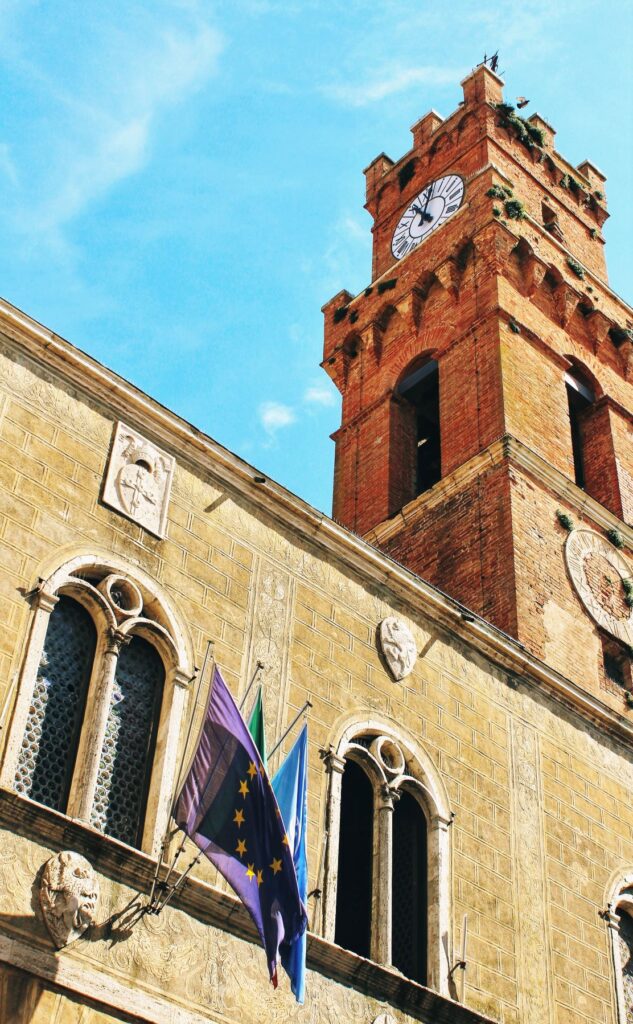 red tower with tuscan flags in pienza