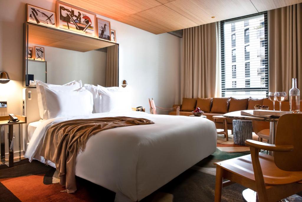 Modern Paris hotel suite with a large white bed, warm wood finishes, floor to ceiling windows, and a comfortable seating area. Contemporary spaces like this are a hallmark of many of the best boutique hotels in Paris.