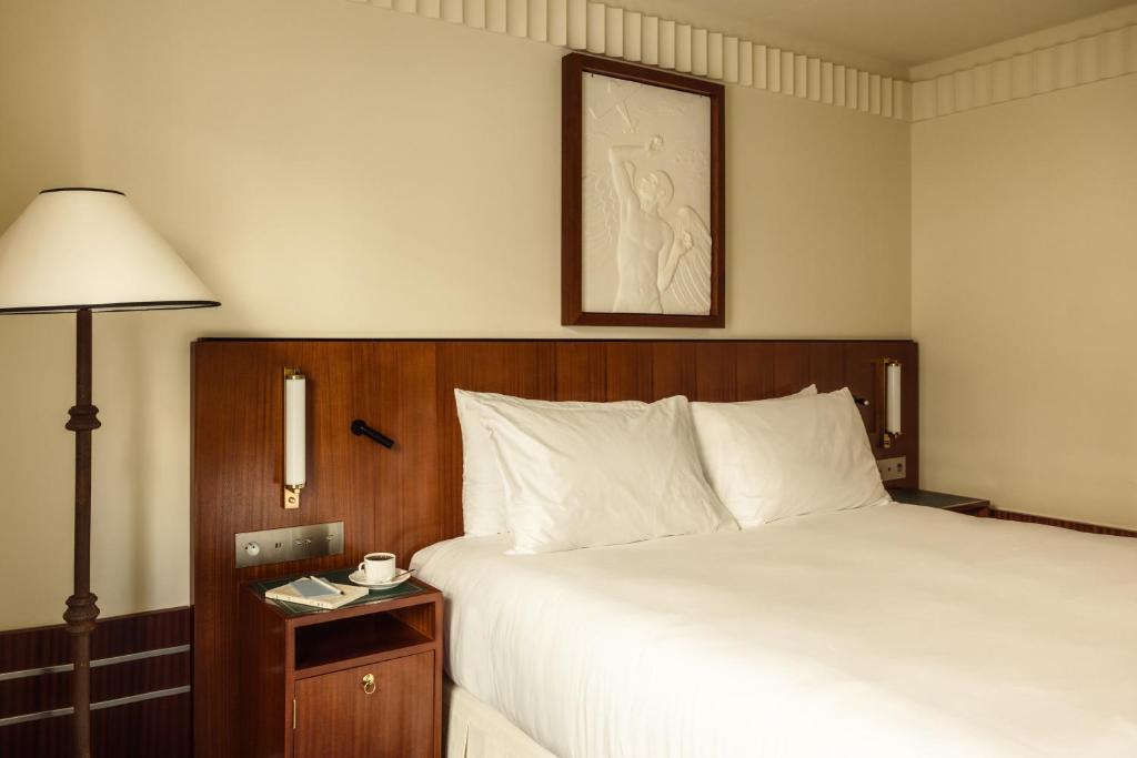 Classic luxury boutique Paris hotel room with warm wood furnishings, white linens, and understated decor creating a calm and comfortable retreat.