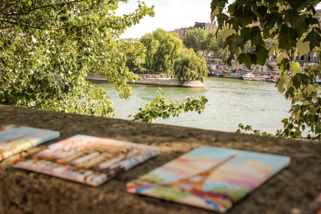 pieces of art on stone wall with view of the Seine and the tip of the island where you will find the paris garden under willow trees
