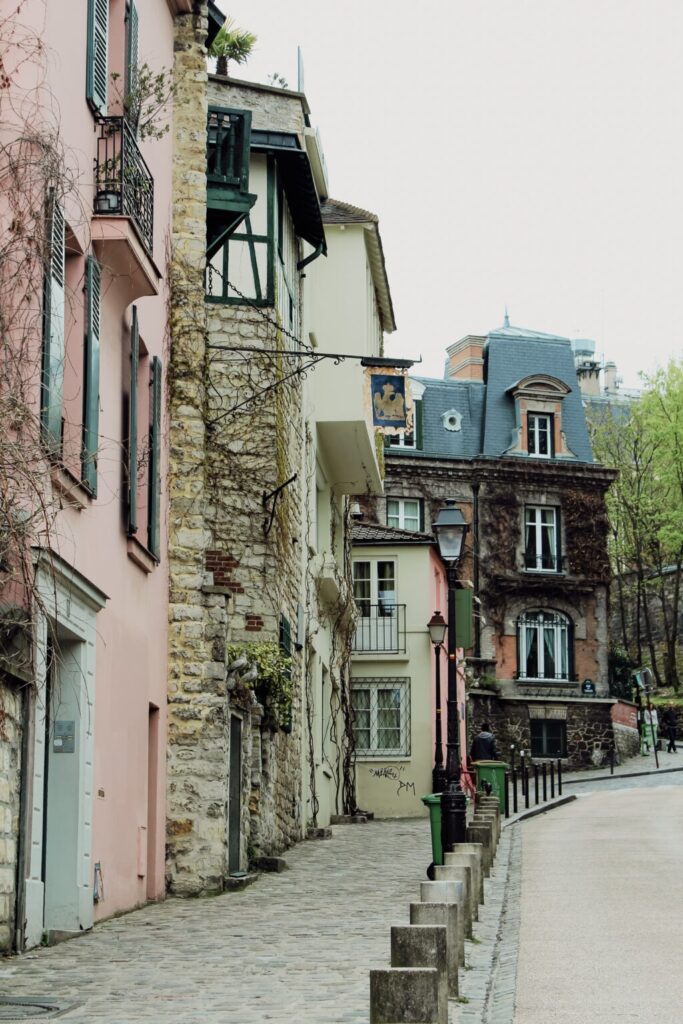 Montmartre street lined with pastel buildings, stone walls, and historic architecture under a blue sky. Wandering charming neighbourhoods like this is one of the most romantic places in Paris.