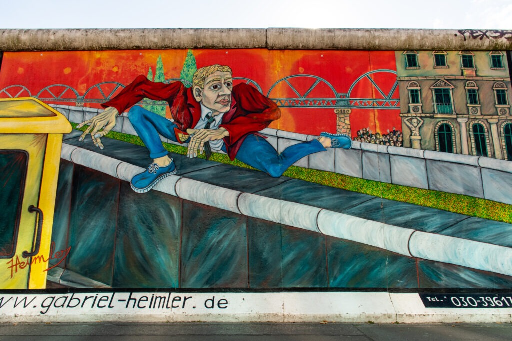wall with artwork of man jumping over berlin wall is what berlin is known for
