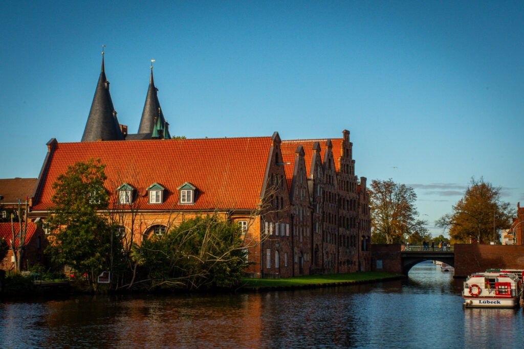 river with tall buildings on bank and boat as things to do Lübeck