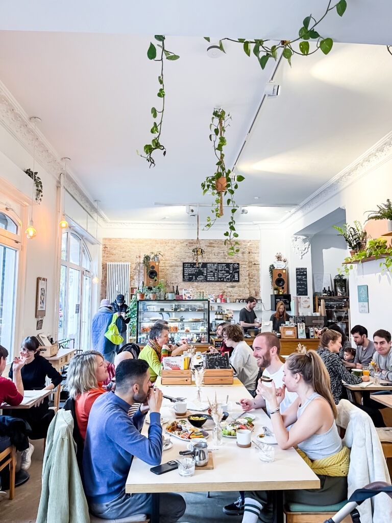 vegan cafe in berlin with tables and chairs, people eating and plants