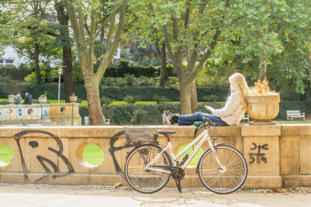 girl reading book and bike leaning on stone wall in best parks in berlin germany