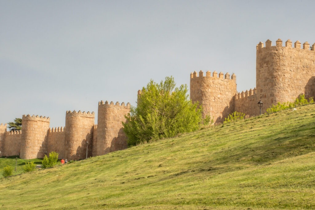 slopping green grass to wall fortress with 5 rounded towers on a day trip to avila from madrid