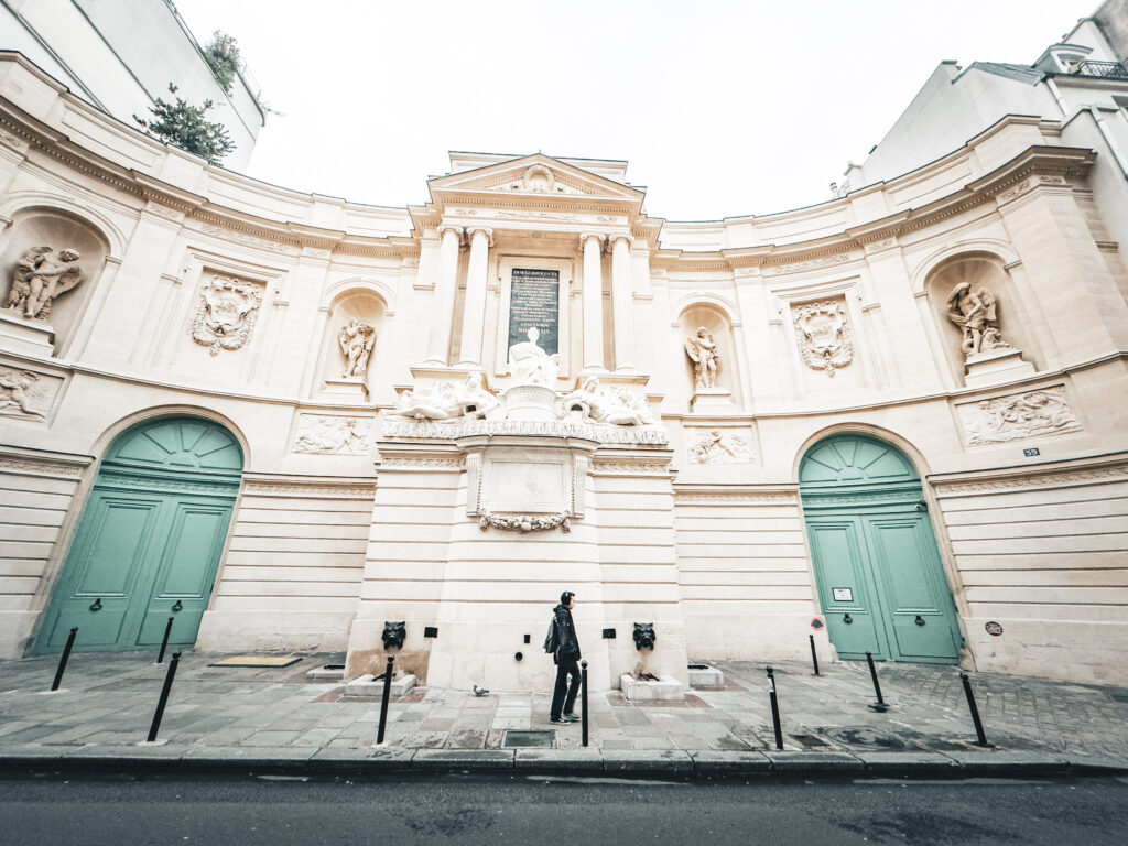 white museum with fountain and two teal doors with slow traveller walking on street in paris 