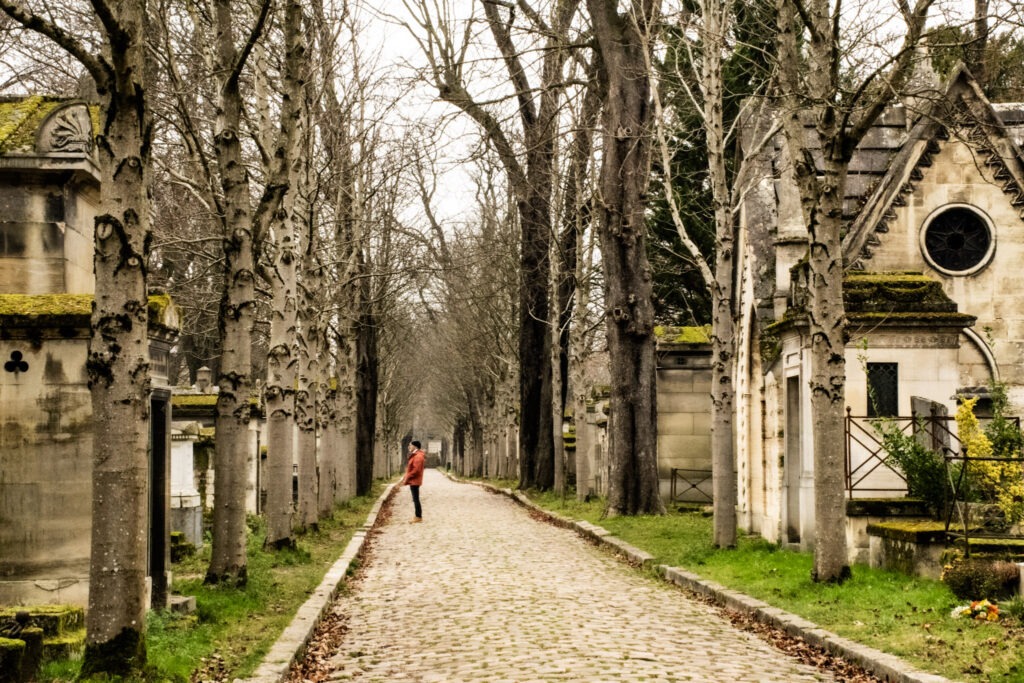 cobblestone lane with trees and tombstone with man standing while on the pere lachaise cemetery tour