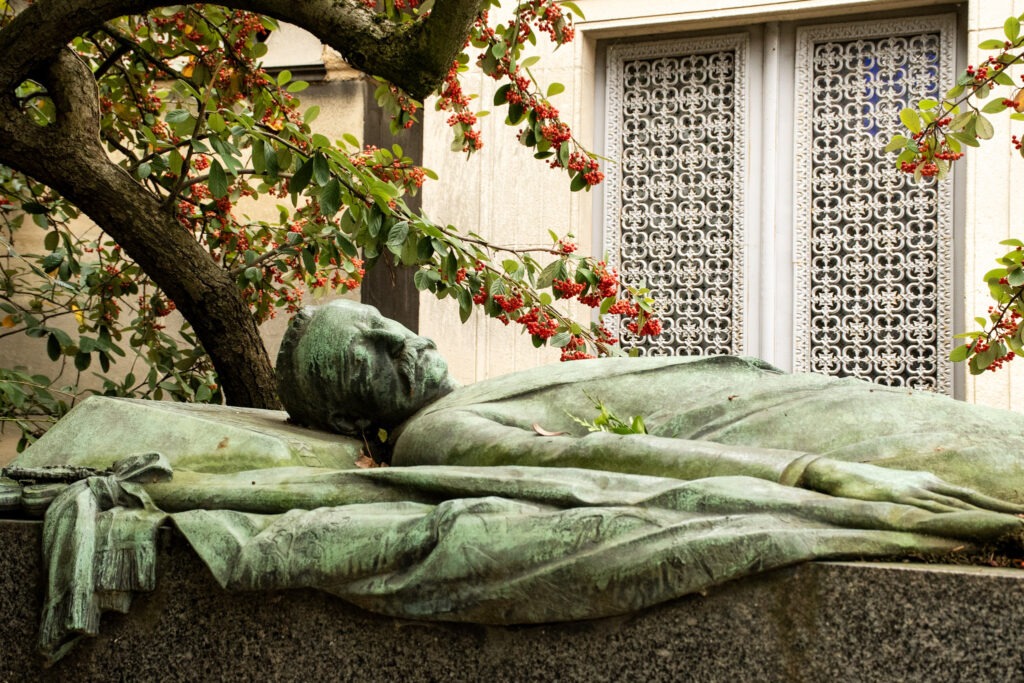 bronze statue above on grave site with tree in pere lachaise cemetery in paris