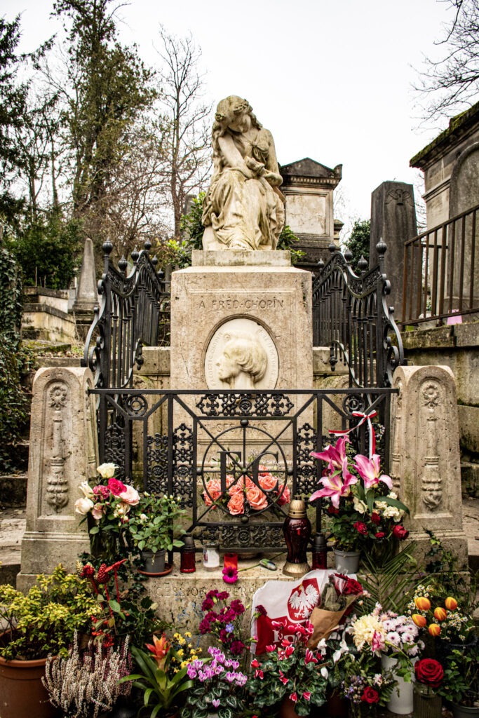 flowers at bottom of stone statue of grave at pere lachaise cemetery in paris