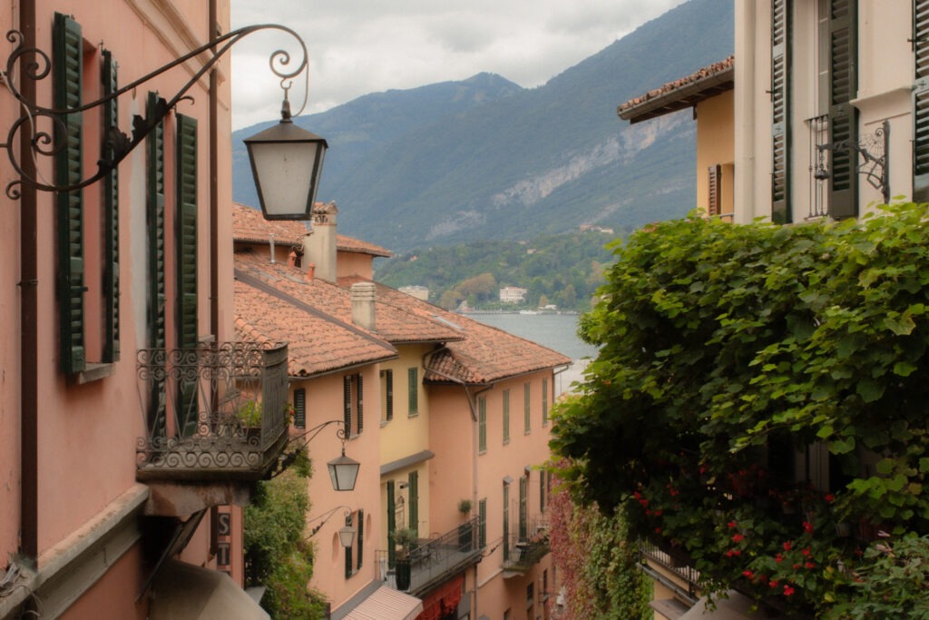 pink building with green shutters and lantern with faint view to lake como and mountains