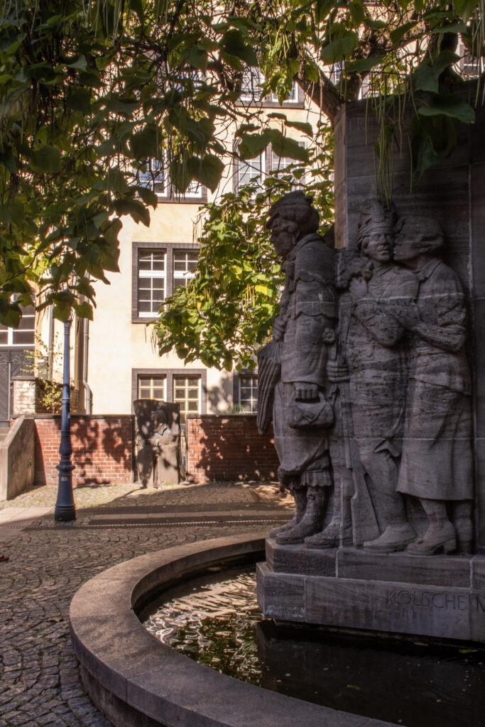 What to See + Do in Cologne in One Day 6 While on a one day Cologne itinerary wander the Old Town for this fountain under a tree canopy