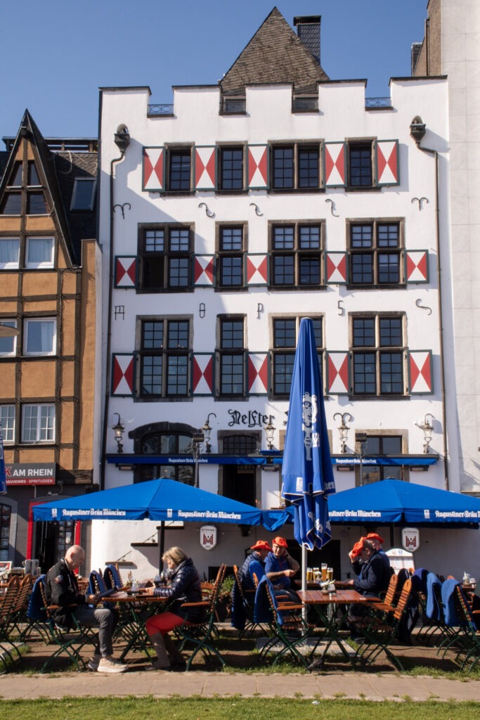 tall white building with blue umbrellas at table and chairs in cologne germany
