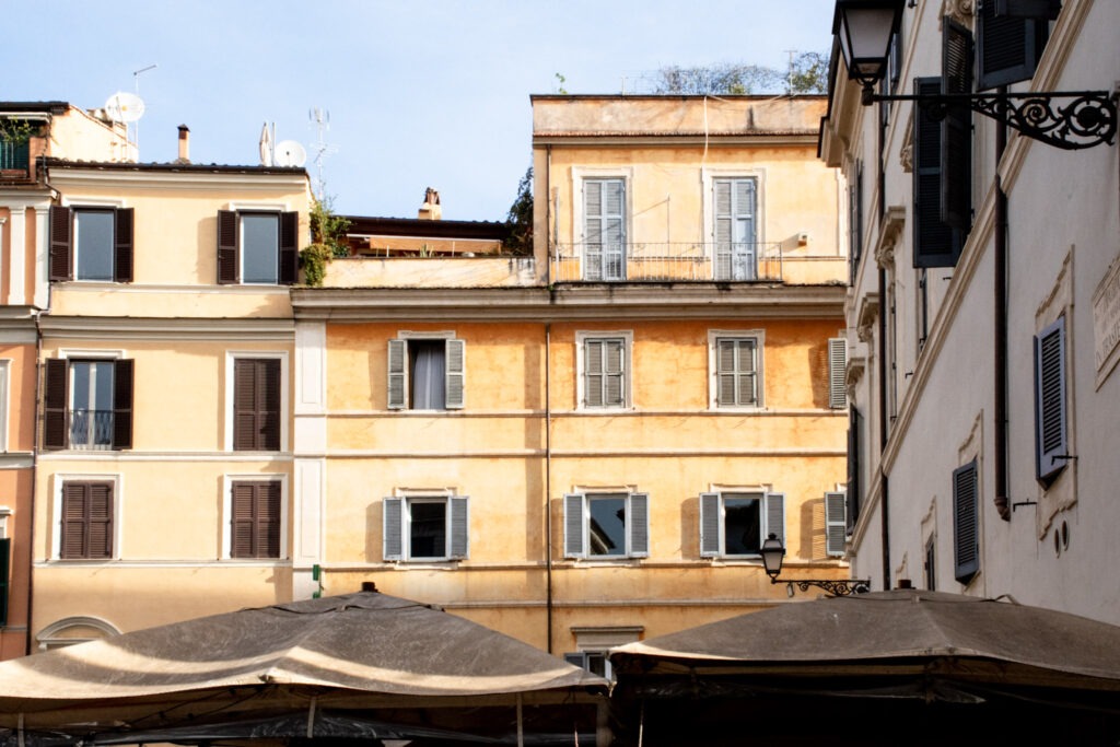 buildings in yellow with gray shutters with umbrellas under while in Trastevere Rome