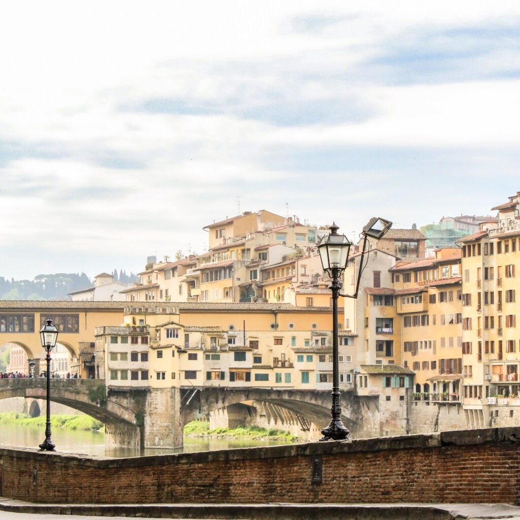 view of the wall lining the Arno river in florence with view to the bridge and colourful buildings