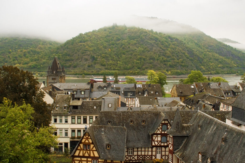 view of the rooftops in bacharach with rhine river, a riverboat and mountains