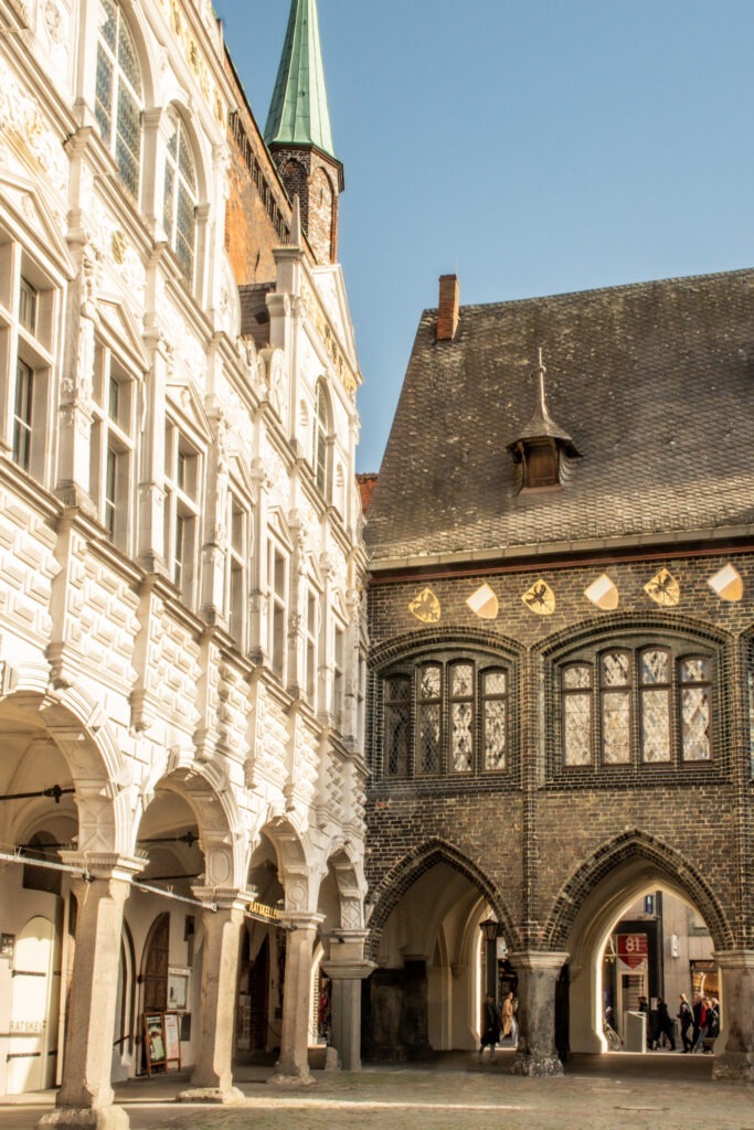 Visit Lubeck's rathaus, city hall. White facade with arches connected with black brick facade with steep roof
