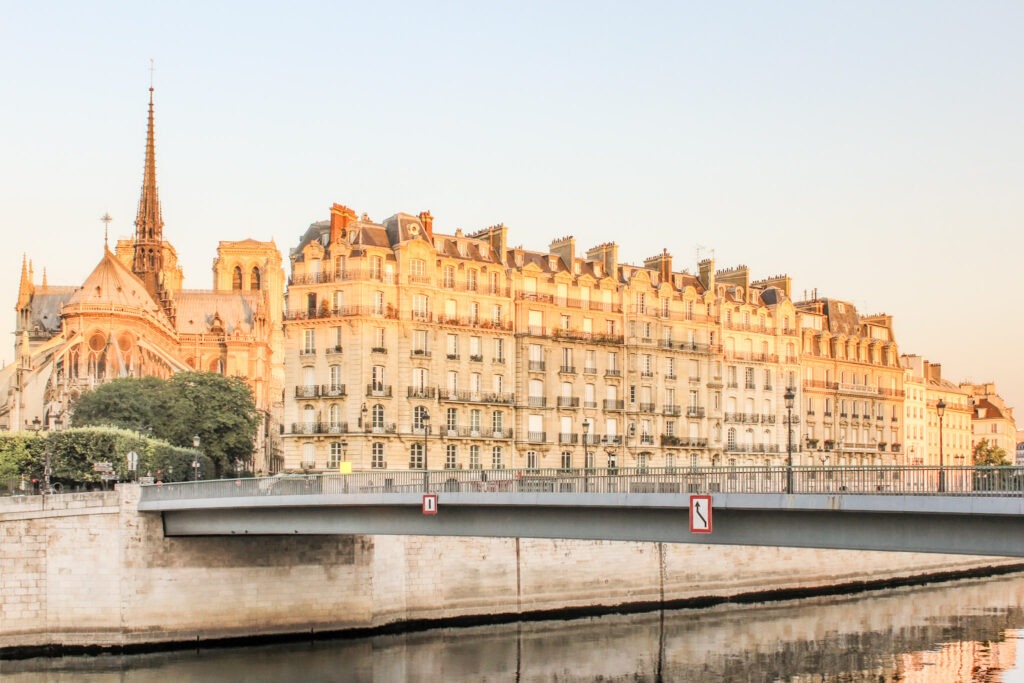 Warm sunset light reflects across historic Paris apartment buildings beside the river with Notre Dame visible in the background. The scenic riverside view shows why many travelers recommend spending several days in Paris to fully enjoy the city atmosphere.