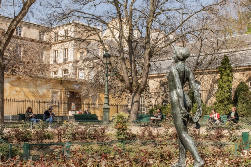 Statue in colorful flower beds and historic buildings in le marais. Relaxing in Paris's squares and gardens is an easy way to balance sightseeing during a 4 day Paris itinerary.