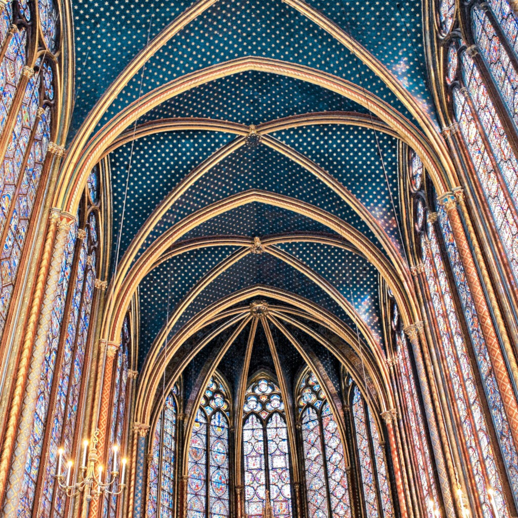 Vaulted blue ceiling covered in gold stars rises above colorful stained glass windows inside Sainte Chapelle. The remarkable interior makes this Gothic chapel a memorable addition to a 4 day Paris itinerary.
