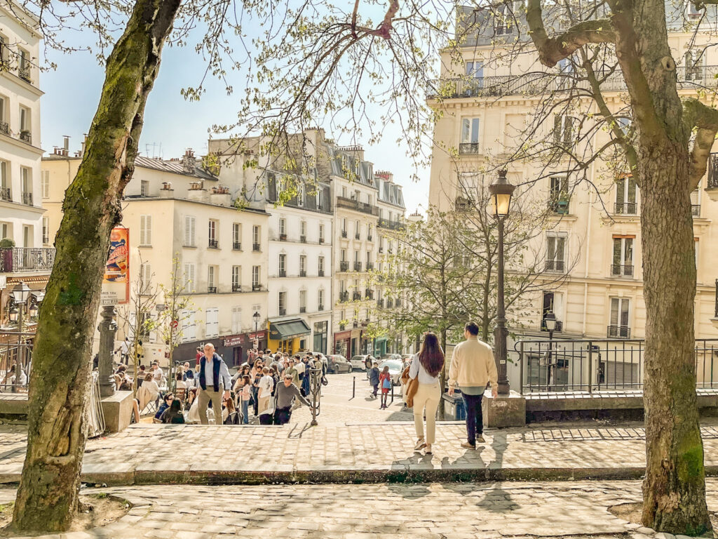 Visitors gather at a scenic overlook in Montmartre surrounded by trees and classic Paris architecture on a sunny afternoon. The neighborhood's elevated views and lively atmosphere make it a worthwhile stop on a 4 day itinerary in Paris.