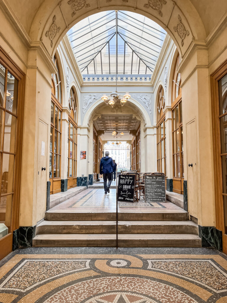 Elegant covered passage with mosaic floors, glass ceiling, and café seating creates a timeless Paris atmosphere. Hidden passages like this offer unique discoveries for travelers spending 4 days in Paris.