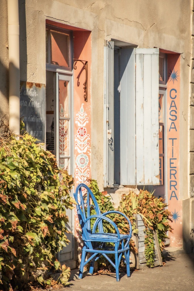 Bright blue chairs outside Casa Terra, an interior design atelier in L’Isle-sur-la-Sorgue, with decorative painted flowers, pale blue shutters, and climbing greenery. One of the independent design shops that add to the town's appeal for interiors enthusiasts.
