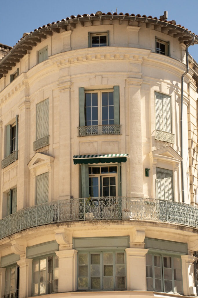 Elegant limestone corner building with pale green shutters and wrought-iron balconies in Avignon, Provence.