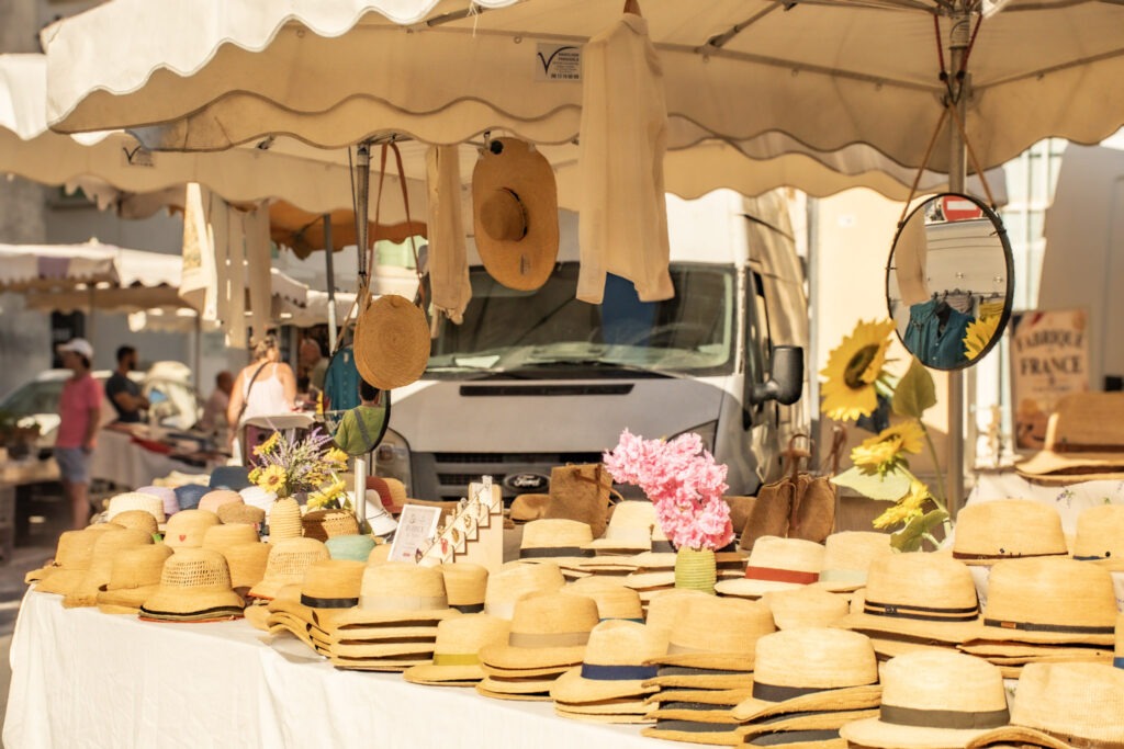 L'Isle-sur-la-Sorgue market stall showing a table with rows of straw hats made in Provence. 