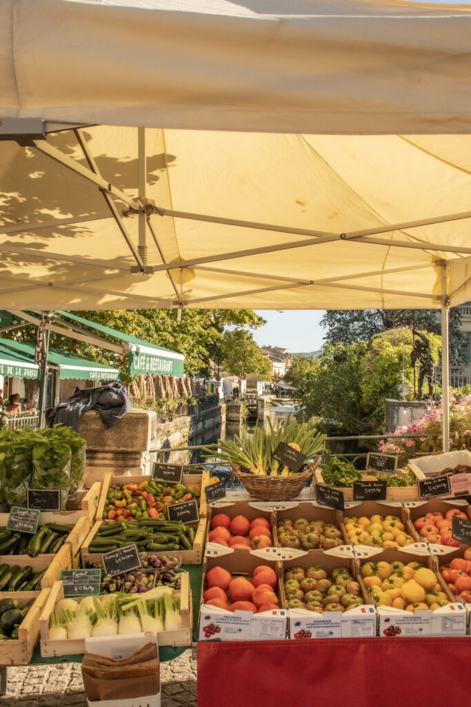 Fresh fruit and vegetable stalls beneath canvas awnings at the Sunday market in L’Isle-sur-la-Sorgue, Provence.