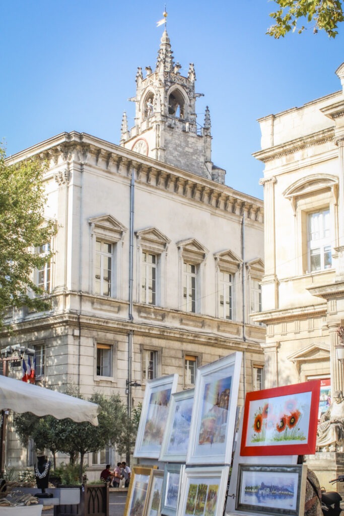Framed paintings and artwork displayed at an outdoor market near Avignon's historic town hall in Provence.