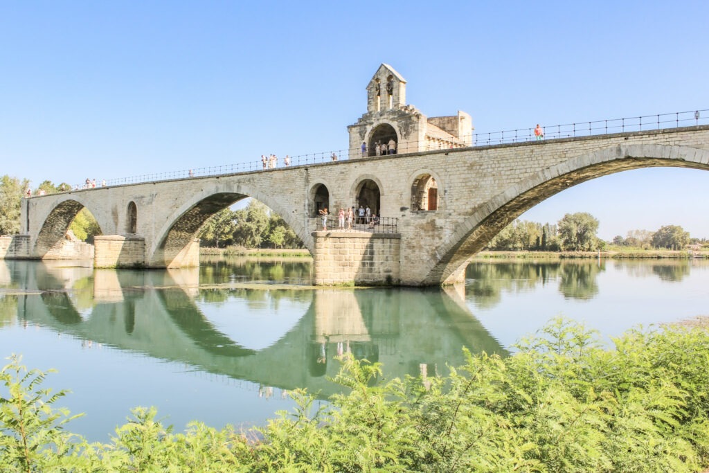 Stone arches of the Pont Saint-Bénézet bridge reflected in the Rhône River in Avignon, France.