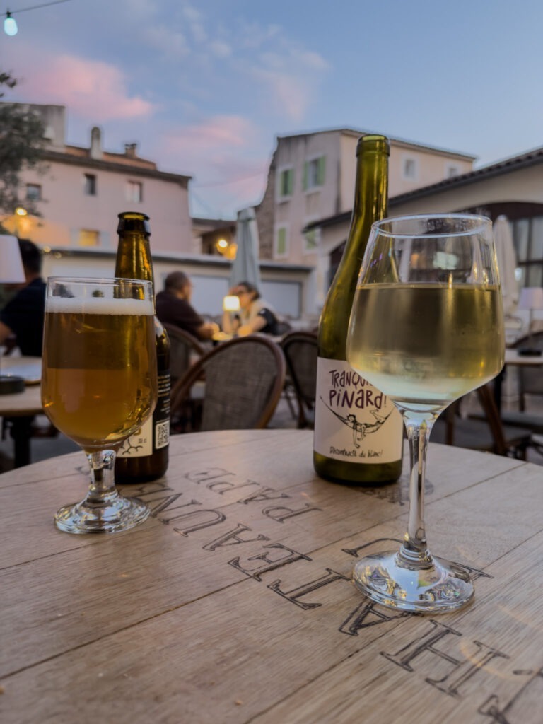 Glass of white wine and beer on an outdoor café table at dusk in L’Isle-sur-la-Sorgue, Provence.