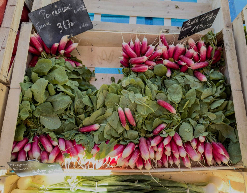 Bunches of fresh pink and white radishes displayed in wooden crates at the L’Isle-sur-la-Sorgue Sunday market.