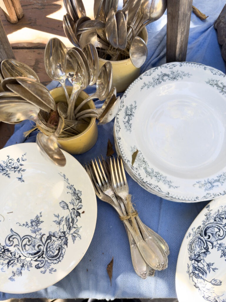 Vintage silver cutlery and blue-and-white patterned porcelain plates displayed at the L’Isle-sur-la-Sorgue antiques market.