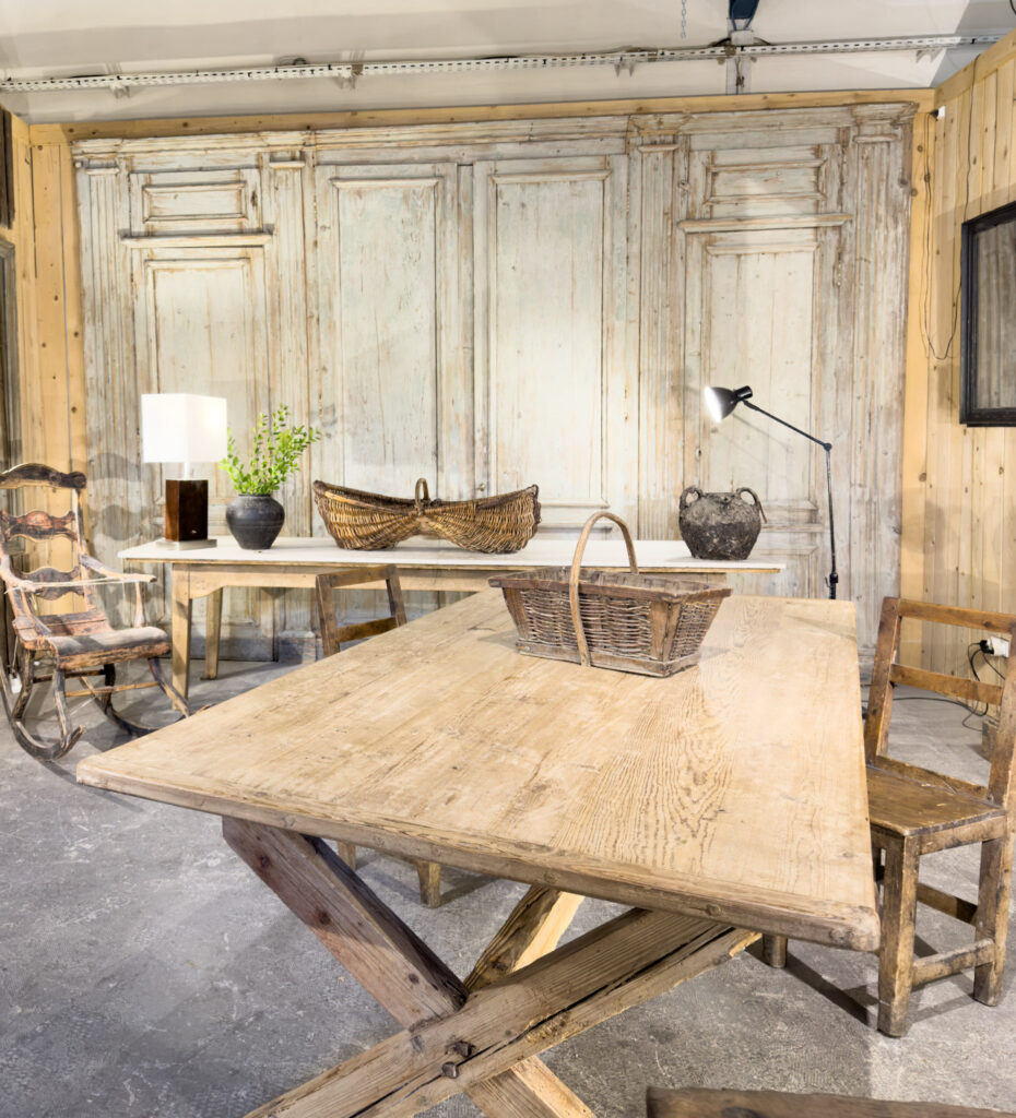 Large rustic wooden dining table with antique chairs and weathered wood panelling at an antique dealer in L’Isle-sur-la-Sorgue.