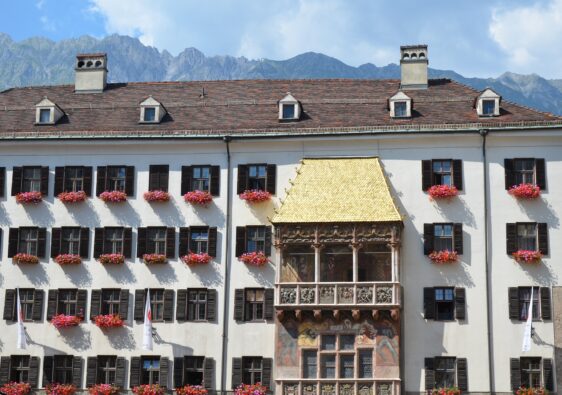 white building with pink flowers in window boxes with mountains in Innsbruck Old Town