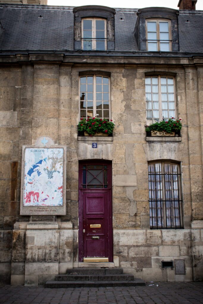 ancient building with red door and windows with flowers at the side of church in saint germain district