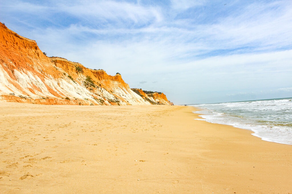 sandy beach with water and red cliffs in algarve 