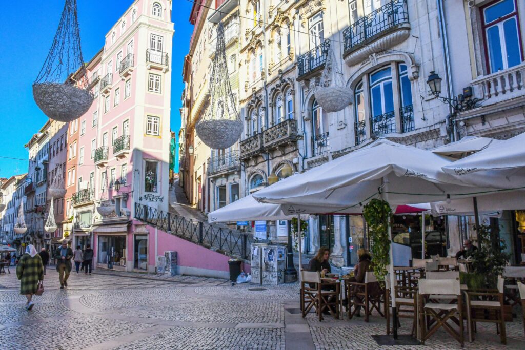 cobbled street with cafe table and chairs with umbrellas, people walking with tall buildings from a coimbra itinerary