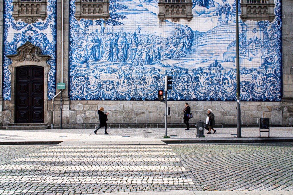 blue tiles on church with people walking by with street and street lamp in porto 